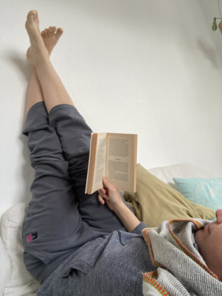 Denise liegend mit den Beinen hoch an der Wand, liest ein Buch