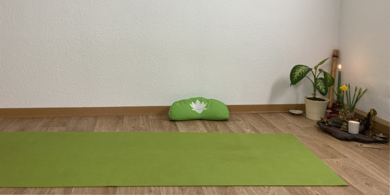 Grüne Yogamatte im Zimmer mit grünem Meditationskissen und kleinem Altar